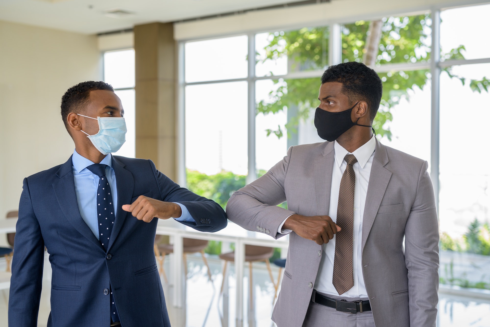 Two African businessman wearing medical mask while greeting with elbow bump greeting at office