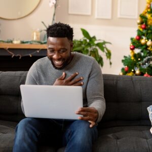 Happy african american man sitting on sofa, having video call, christmas decorations in background