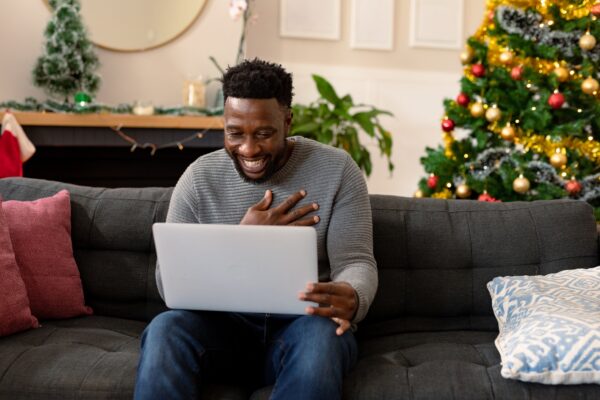 Happy african american man sitting on sofa, having video call, christmas decorations in background